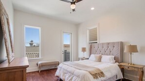 A bedroom with a large bed, a wooden bench, a desk, and a balcony.