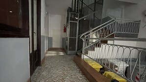 Un couloir doté d’un sol carrelé, d’une rambarde en métal et d’un escalier menant à un niveau supérieur.
