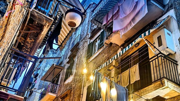 Une rue étroite bordée d’immeubles dotés de balcons et de climatiseurs, illuminée de guirlandes lumineuses et où l’on peut voir du linge séchant aux fenêtres.