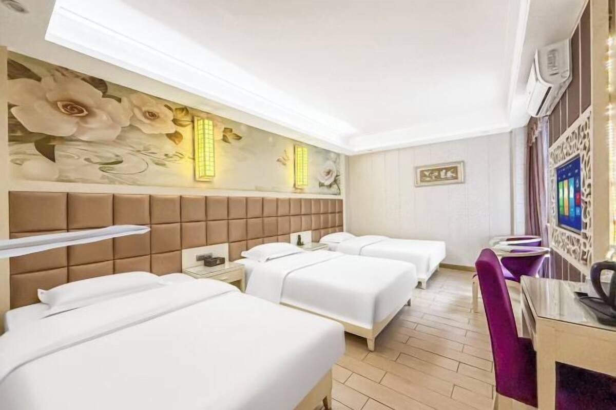 A hotel room with three beds, a large floral mural, a wall-mounted TV, and a wooden floor.