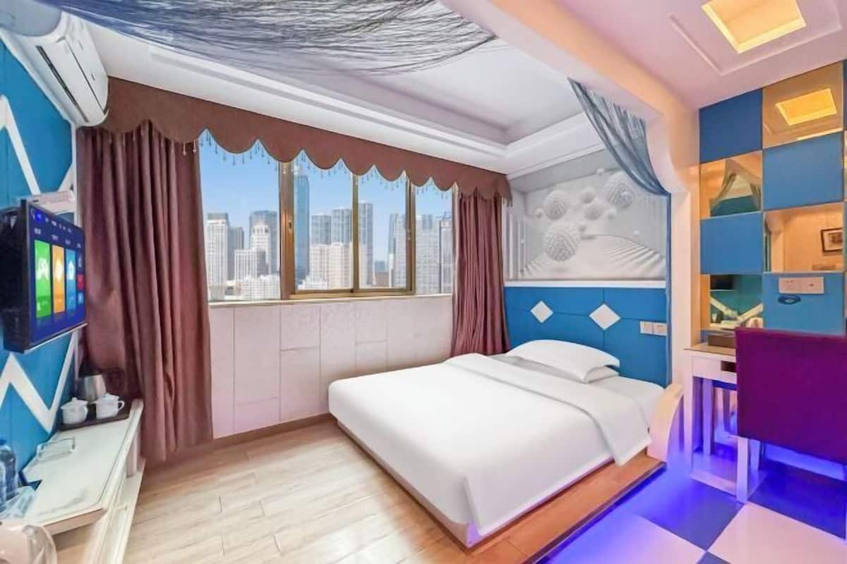A hotel room with a bed, a desk, a chair, and a large window with curtains.