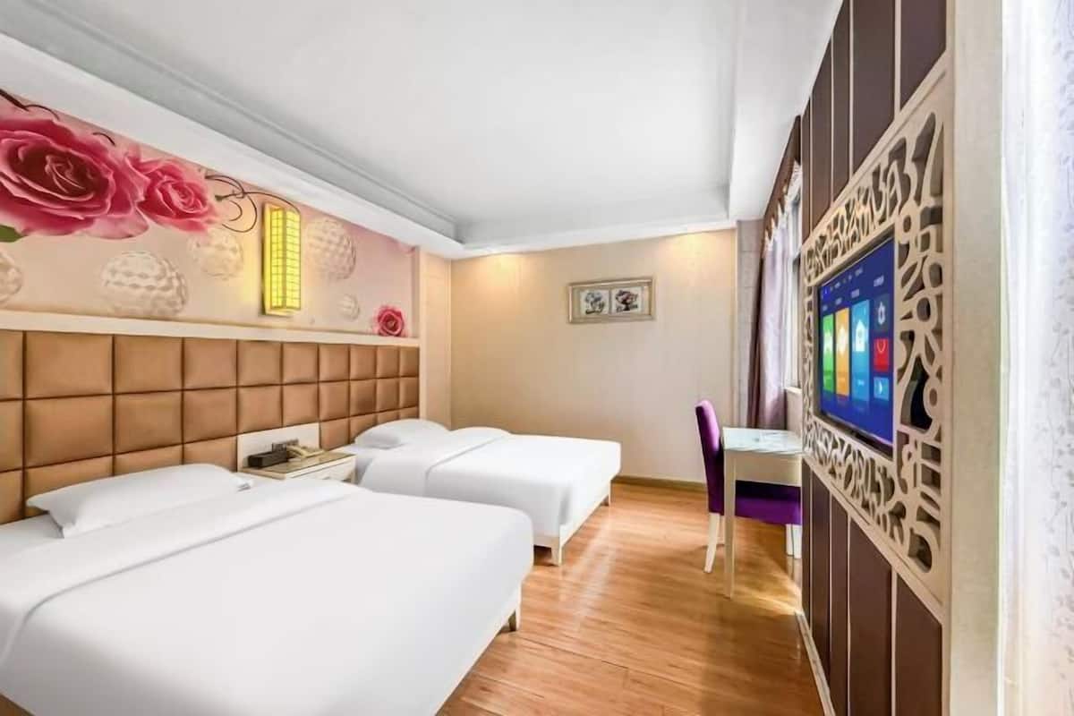A hotel room with two beds, a desk, and a TV.