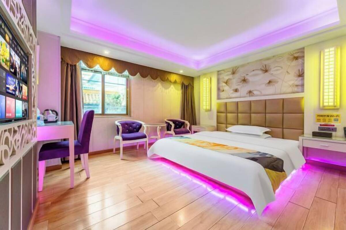 A hotel room with a large bed, a desk, two chairs, a TV, and a window with curtains.