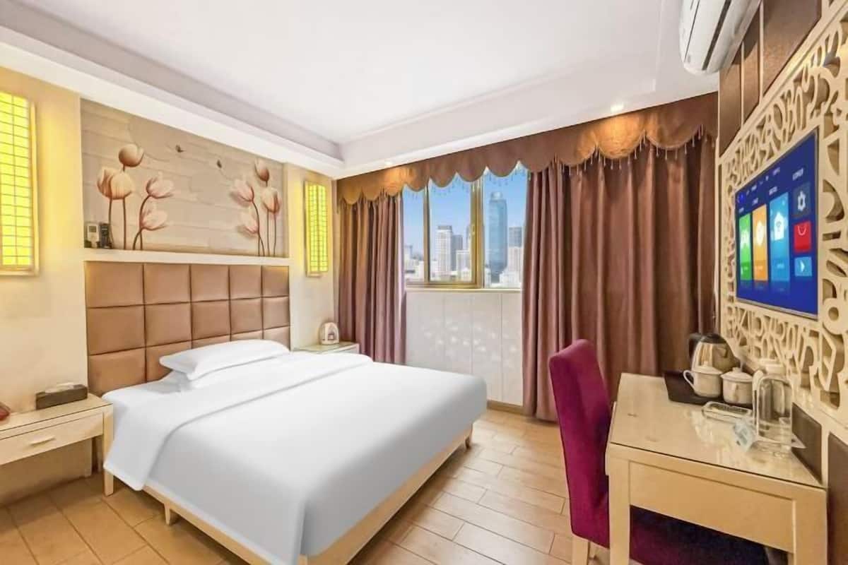 A hotel room with a bed, a desk, a chair, a TV, and a window with curtains.