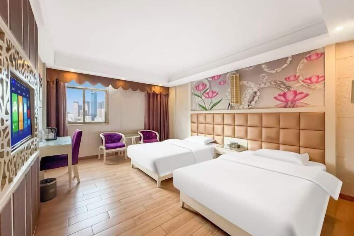 A hotel room with two beds, a desk, a chair, a TV, and a city view.