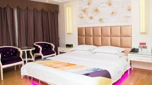 A hotel room with a large bed, two chairs, a small table, and a wall with a floral mural. - City Boutique Hotel (Heshan Zhongshan Road Xintiandi Branch) (Heshan)