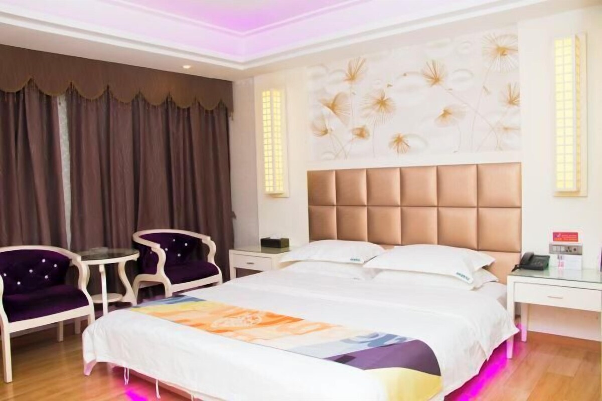 A hotel room with a large bed, two chairs, a small table, and a wall with a floral mural.