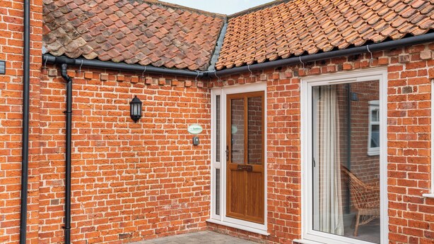 A corner building with a brick facade, a tiled roof, and a wooden door. - The Stables - UK36121 (Horsington)