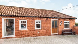 A brick house with a tiled roof, a front door, and a bench outside. - The Stables - UK36121 (Horsington)