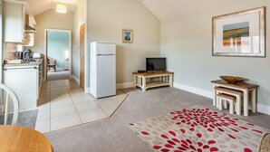 A compact kitchen with a refrigerator, a dining area with a table, and a living space with a television and a framed picture on the wall. - The Stables - UK36121 (Horsington)