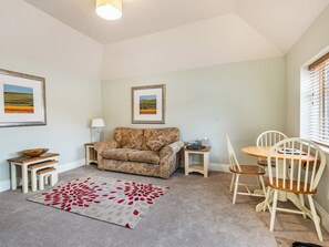 A cozy living room with a floral sofa, a small wooden table, a dining table with chairs, and two framed landscape paintings on the walls. - The Stables - UK36121 (Horsington)