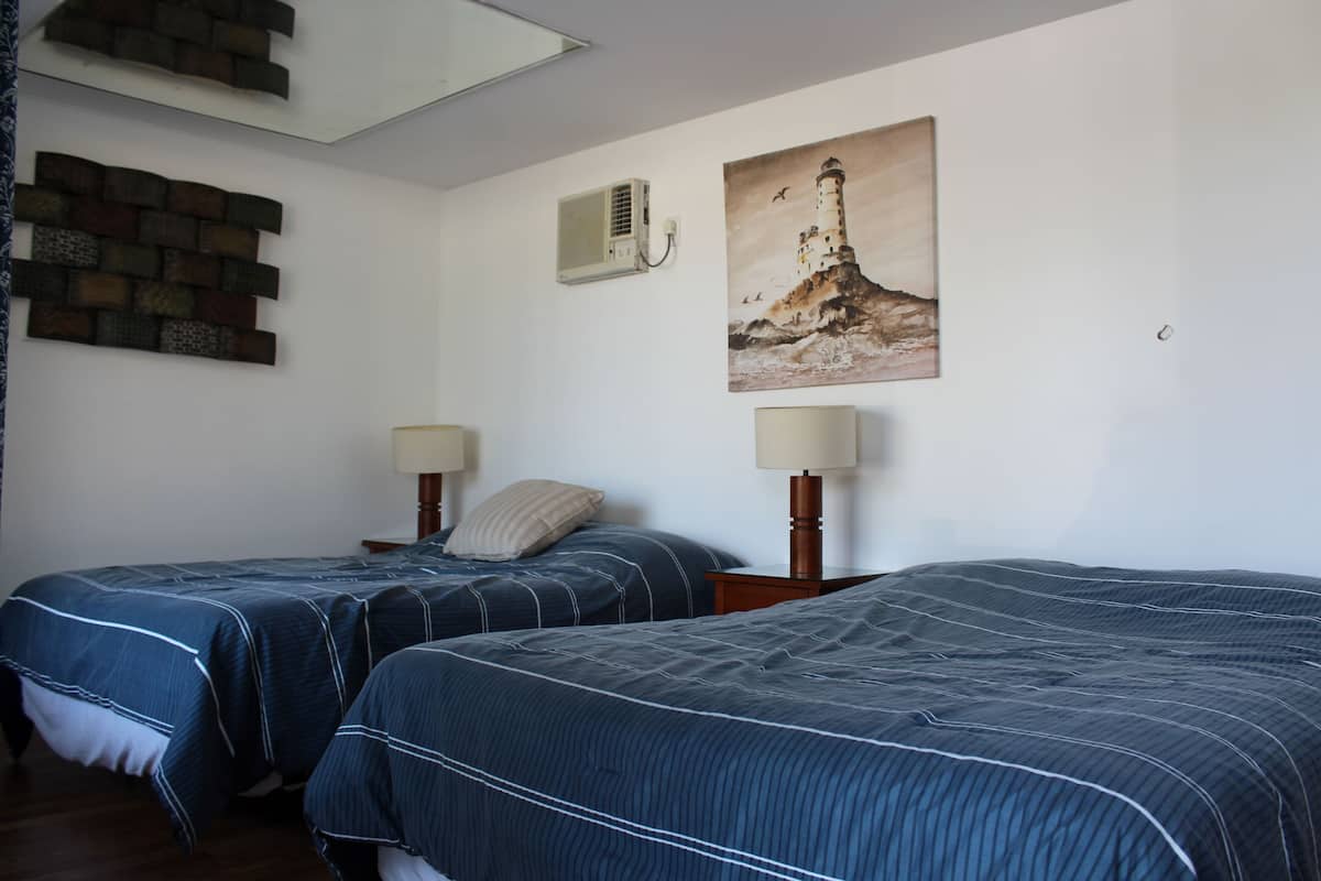 Ein Hotelzimmer mit zwei Betten, Wanddekoration aus Ziegelsteinen, einer Klimaanlage und einem Gemälde eines Leuchtturms.