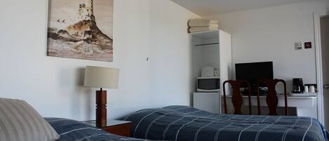 A hotel room with two beds, a painting of a lighthouse, a desk with a television, and a coffee maker.
