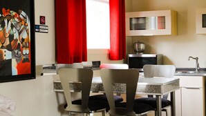 A modern kitchen with a dining area, featuring a painting, red curtains, and contemporary furniture. - Le Marigot (Vaudreuil)