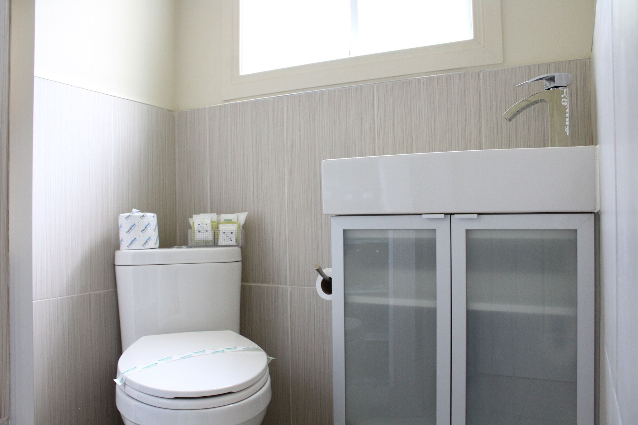 A bathroom with a toilet, a cabinet with frosted glass doors, and a window above the toilet.