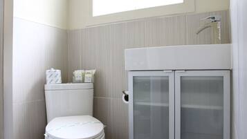 A bathroom with a toilet, a cabinet with frosted glass doors, and a window above the toilet.