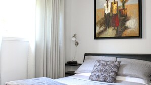 A bedroom with a bed, a nightstand, a lamp, and a painting on the wall. - Le Marigot (Vaudreuil)