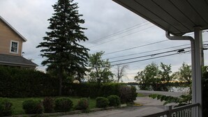 A residential street with a house, a large evergreen tree, and a sidewalk. - Le Marigot (Vaudreuil)