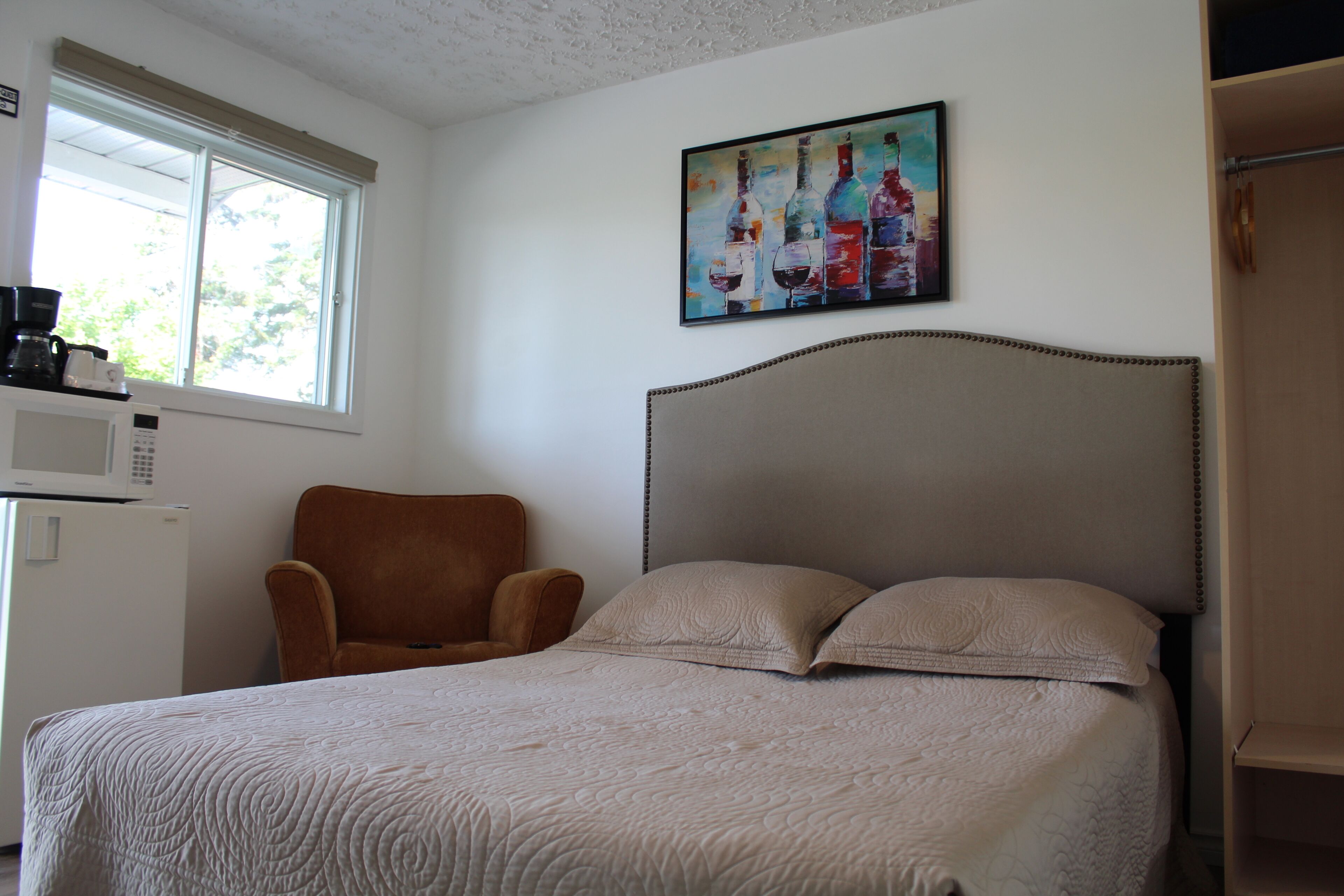 A bedroom with a bed, a chair, a painting, and a microwave.