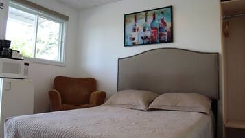 A bedroom with a bed, a chair, a painting, and a microwave.