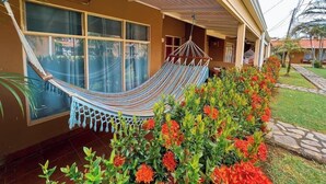 A house with a hammock on the porch, large windows, and a garden with colorful flowers.