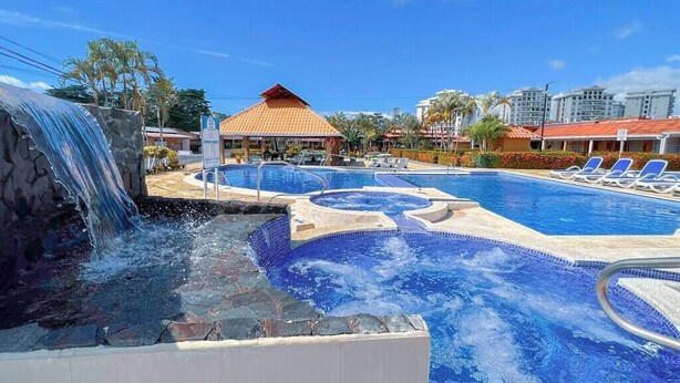 A pool area with a waterfall feature, lounge chairs, and a covered pavilion.