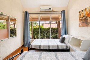 Une chambre à coucher comprenant un lit, un bureau, une fenêtre avec des rideaux et un appareil de climatisation.