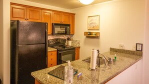 A kitchen with wooden cabinets, a black refrigerator, a microwave, an oven, and a granite countertop. - Grand Sierra Lodge: Walk to Village Gondola & Ski Back Trail (Mammoth Lakes)