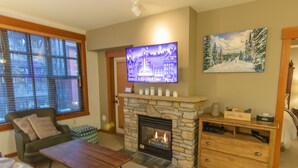A living room with a stone fireplace, a television mounted above it, and a painting on the wall. - Grand Sierra Lodge: Walk to Village Gondola & Ski Back Trail (Mammoth Lakes)