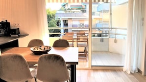 Un balcón con una mesa y sillas, una puerta corrediza de vidrio y vistas a edificios y follaje.