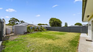A backyard with a lawn, a fenced area, and a building with a flat roof. - Comfort behind Crouch In CBD, newly renovated, perfect for the family & pets (Mount Gambier)
