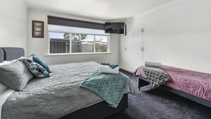 A bedroom with a large bed, a smaller bed, a TV mounted on the wall, and a window with a view of the outside. - Comfort behind Crouch In CBD, newly renovated, perfect for the family & pets (Mount Gambier)