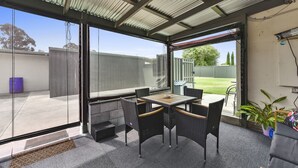 A covered outdoor patio with a table and chairs, a potted plant, and a view of the backyard. - Comfort behind Crouch In CBD, newly renovated, perfect for the family & pets (Mount Gambier)