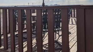 A wooden deck with a large umbrella, outdoor seating, and a view of the sky and distant landscape.