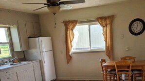 A kitchen with wooden flooring, a refrigerator, a stove, a dining table with chairs, and a ceiling fan.