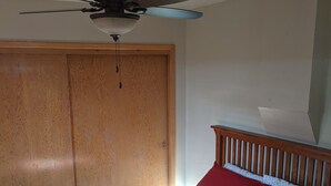 A bedroom with a bed, a wooden wardrobe, a ceiling fan, and a window.