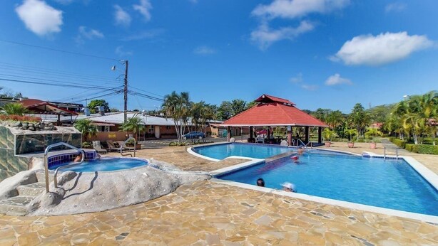 A swimming pool area with multiple pools, stone flooring, and a covered seating area. - Mango Paradise · Steps from the Beach & Fast Wi-Fi (Jacó)