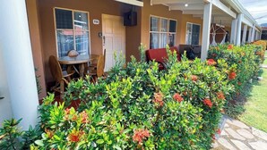 A covered outdoor seating area with tables and chairs, surrounded by lush greenery and flowering plants. - Mango Paradise · Steps from the Beach & Fast Wi-Fi (Jacó)