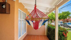 A covered balcony with a hammock, a tiled floor, and a view of the street. - Mango Paradise · Steps from the Beach & Fast Wi-Fi (Jacó)
