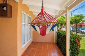 A covered balcony with a hammock, a tiled floor, and a view of the street.