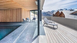 Ett modernt utomhusområde med en pool, ett trädäck, solstolar och utsikt över bergen.