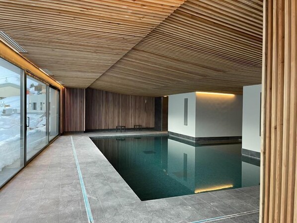 Una piscina interior moderna con techo de madera y paredes de cristal.