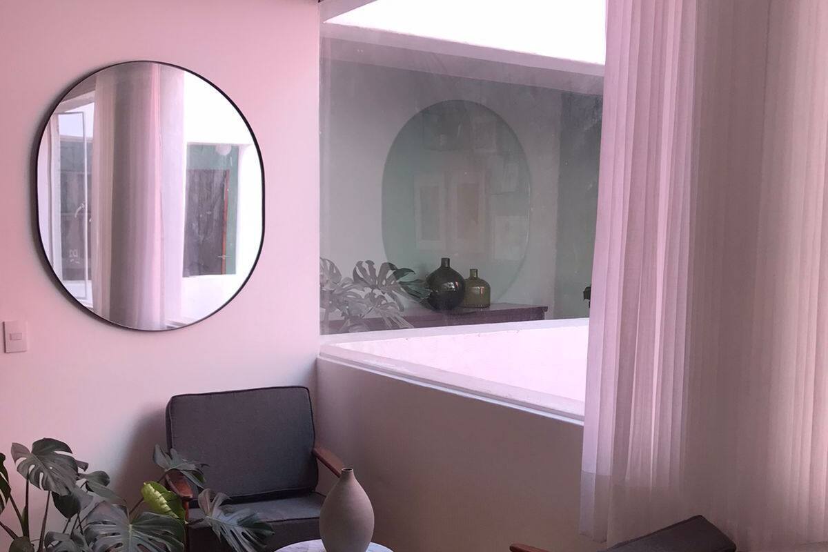 Ein Zimmer mit einem runden Spiegel, zwei Stühlen, einem kleinen Tisch und einem Fenster mit Vorhängen.