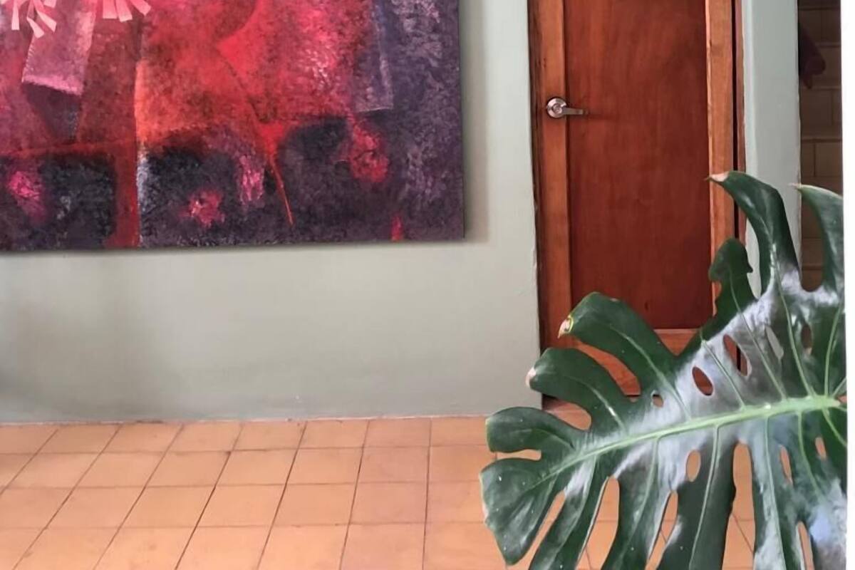 Ein Zimmer mit einem großen abstrakten Gemälde, einer Holztür mit der Aufschrift 'TOILET' und einem Blumentopf.