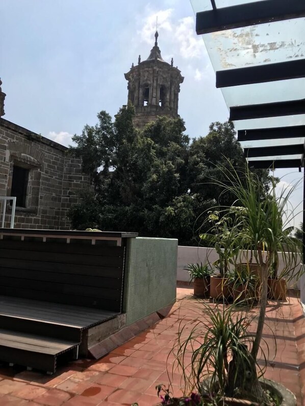 Une terrasse sur le toit offrant une vue sur une tour historique, agrémentée de plantes en pot et donnant sur un bâtiment en pierre.