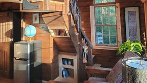 Ein rustikales Blockhaus-Interieur mit einer Holztreppe, einem Globus, einem Kühlschrank und einem Fenster mit Blick auf Bäume.