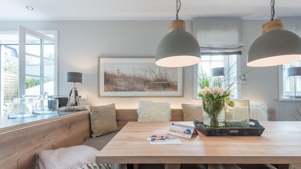 A modern dining area with a wooden table, bench seating, pendant lighting, and a framed landscape painting. - Höög Hüs, Whg. 1 - Höög Hüs (Sylt)