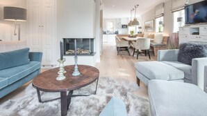 A modern living room with a fireplace, a dining area, and a kitchen in the background. - Höög Hüs, Whg. 1 - Höög Hüs (Sylt)
