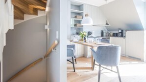 A modern kitchen with white cabinets, a wooden staircase, and a dining area with grey chairs. - Höög Hüs, Whg. 2A - Höög Hüs (Sylt)