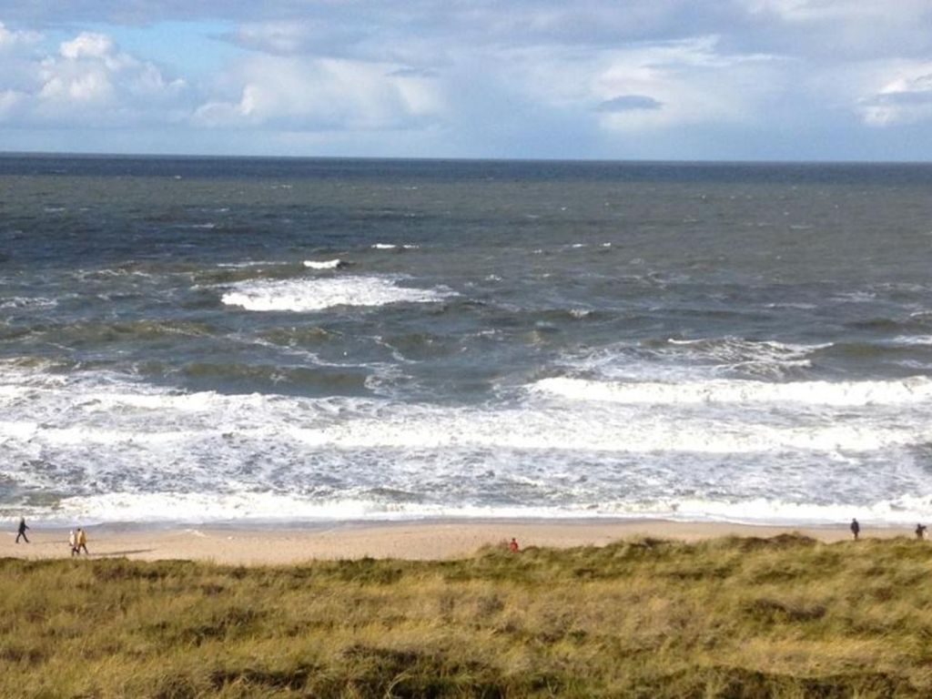 A beach with waves and people walking along the shore.